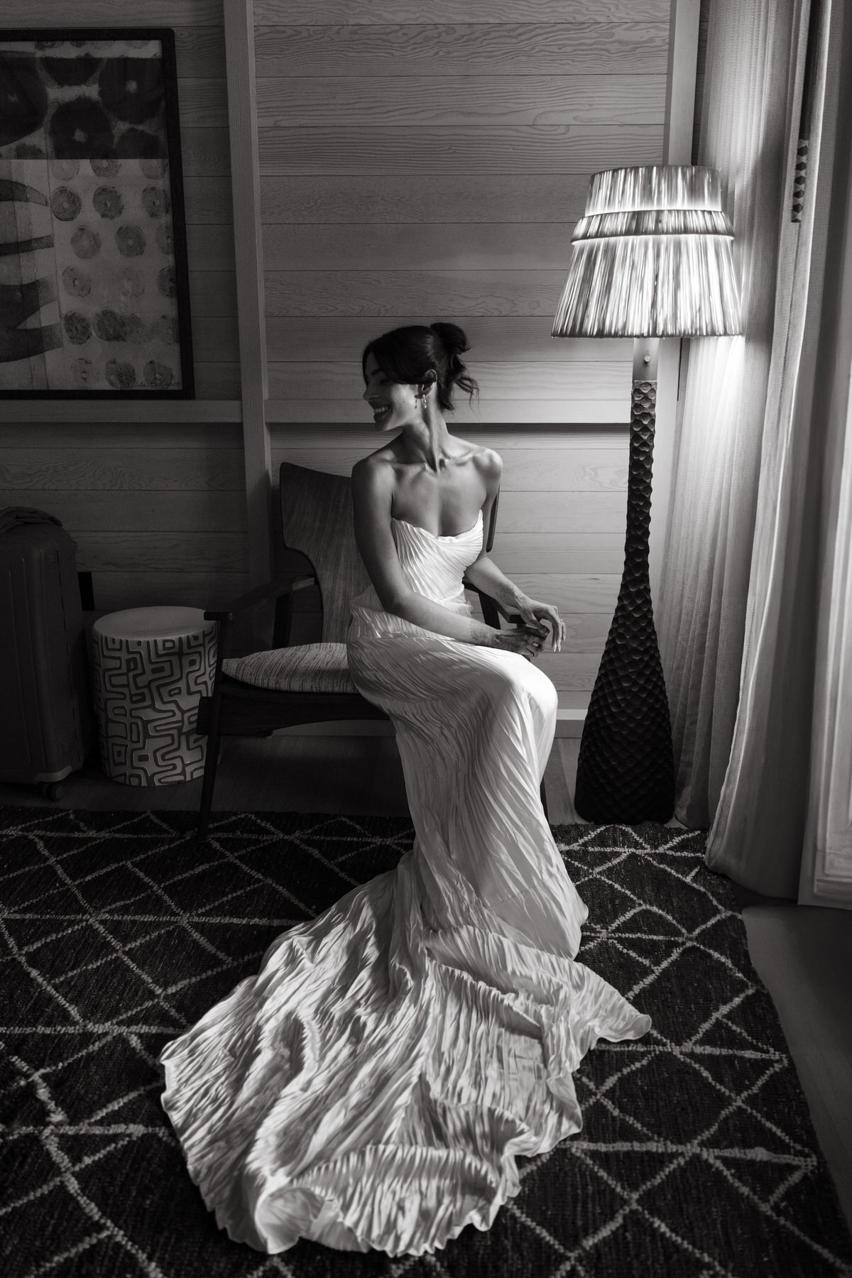 A stunning black-and-white image of the bride sitting elegantly in a chair, her wedding gown flowing around her on the floor. The soft lighting and serene ambiance of the room emphasize the importance of hiring your Oahu wedding vendors in advance to ensure flawless details on your wedding day (and my personal recommendations).