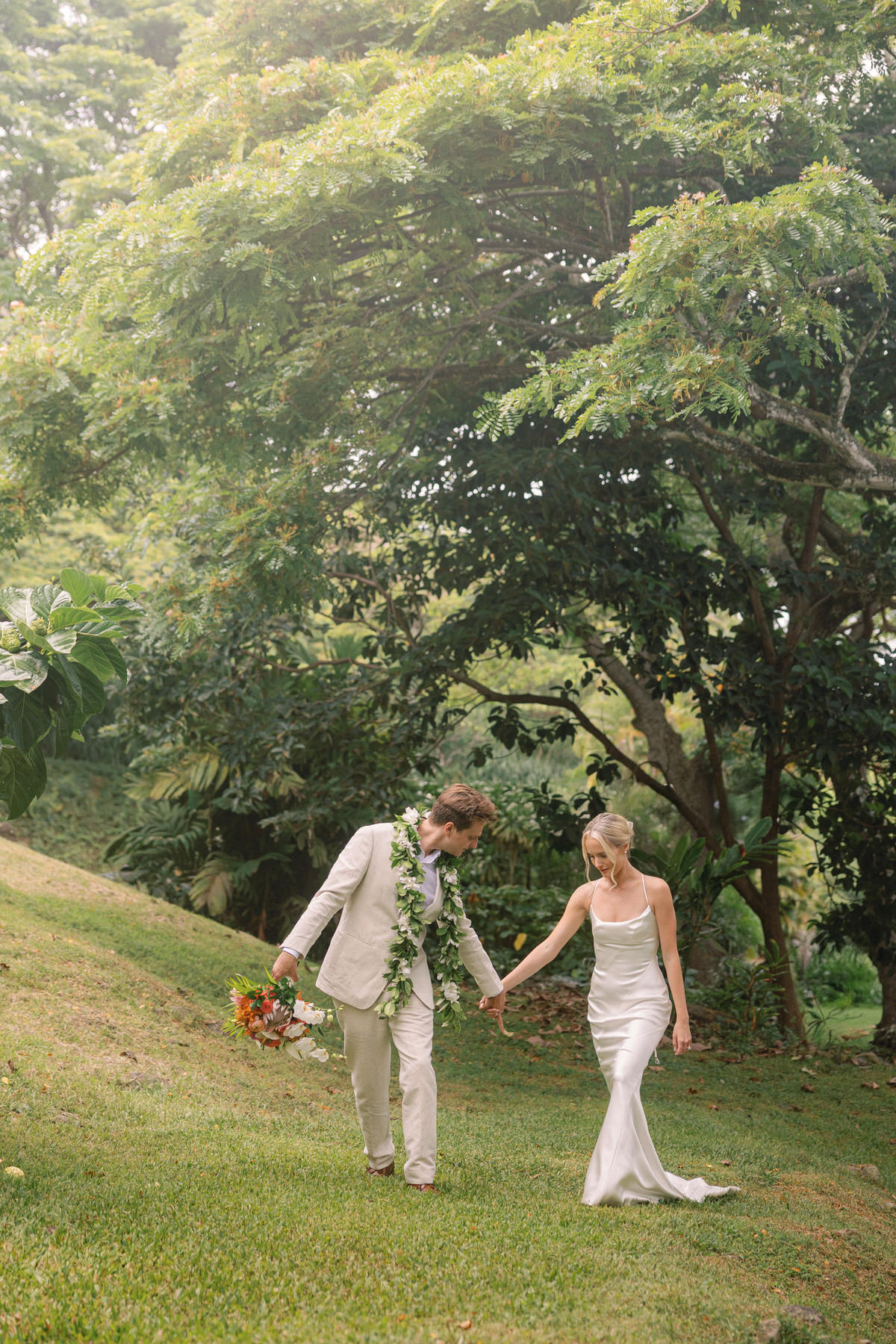 Bride and groom walking hand-in-hand through the lush grounds of Kualoa Ranch, Paliku Gardens, surrounded by greenery