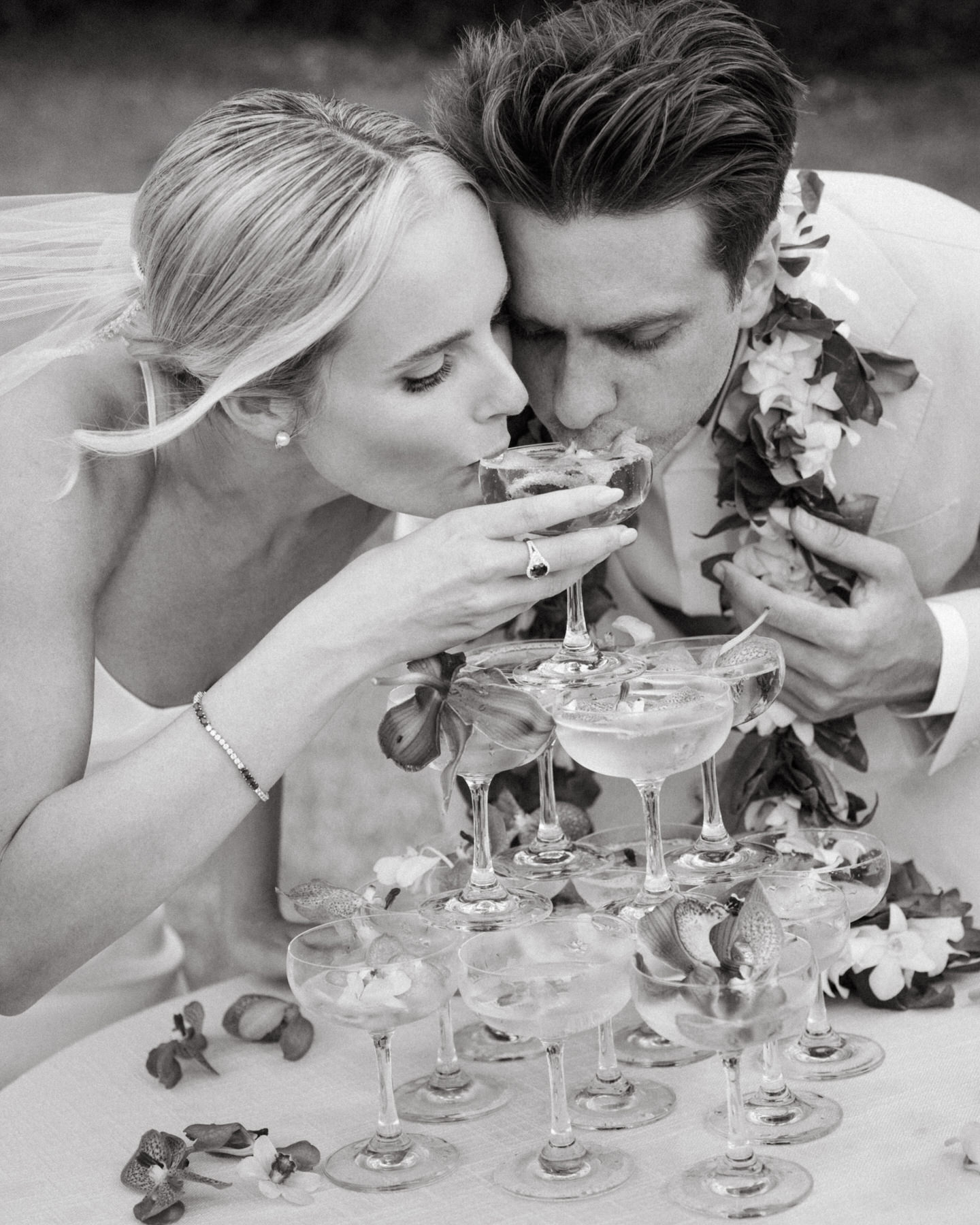 Bride and groom sharing a kiss over a stack of champagne glasses at their wedding at Kualoa Ranch, Paliku Gardens, Oahu