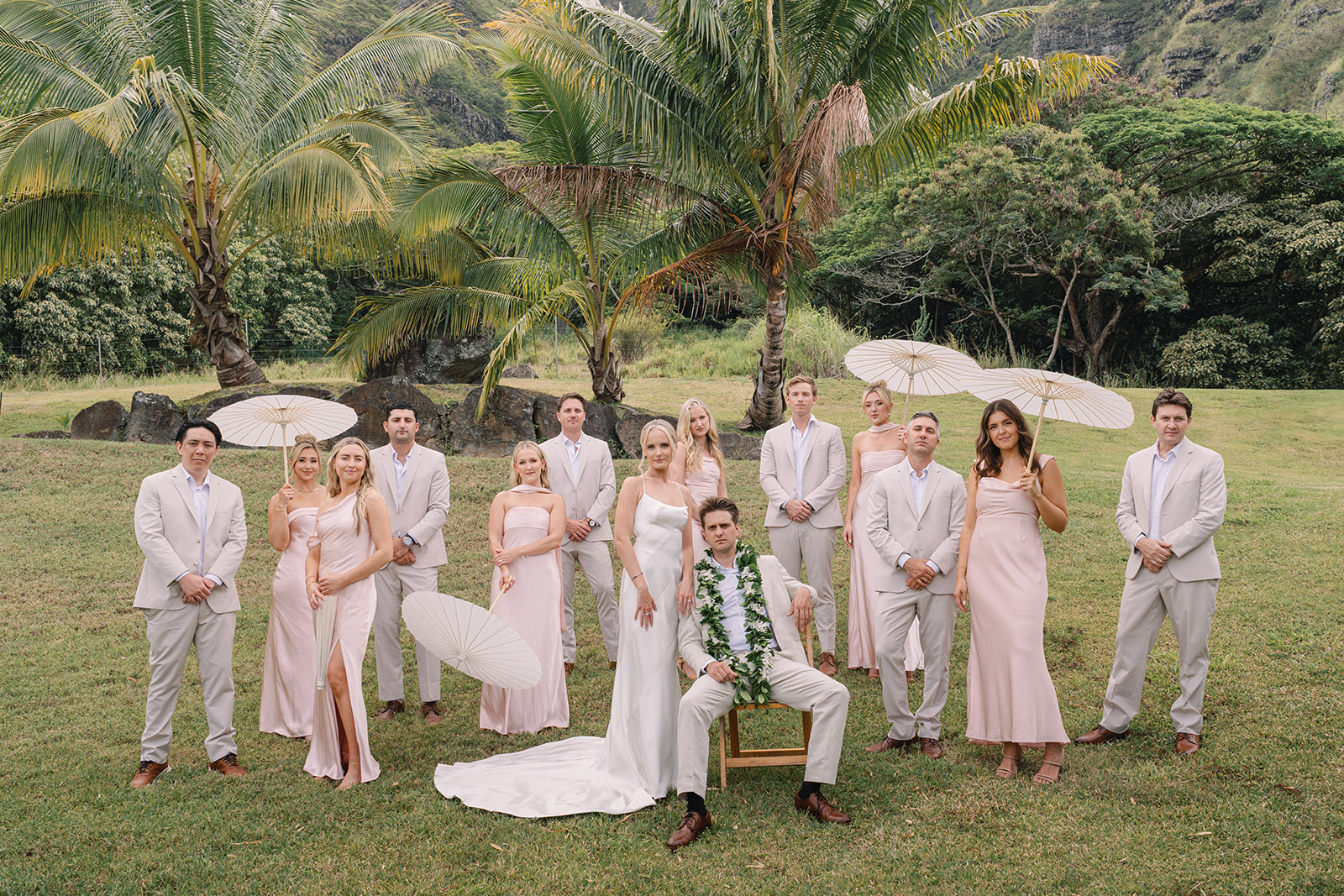 Bridal party and couple posing with parasols at Kualoa Ranch, Paliku Gardens, Oahu, with stunning tropical landscape in the background.