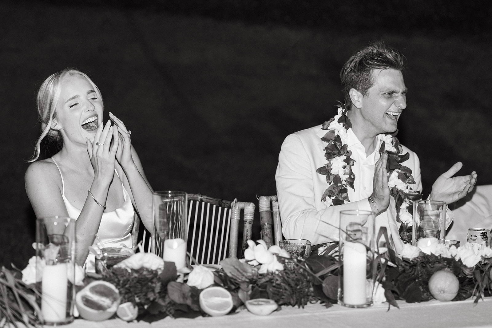 Bride and groom laughing during dinner at Kualoa Ranch, Paliku Gardens, with a floral and candlelit table setting