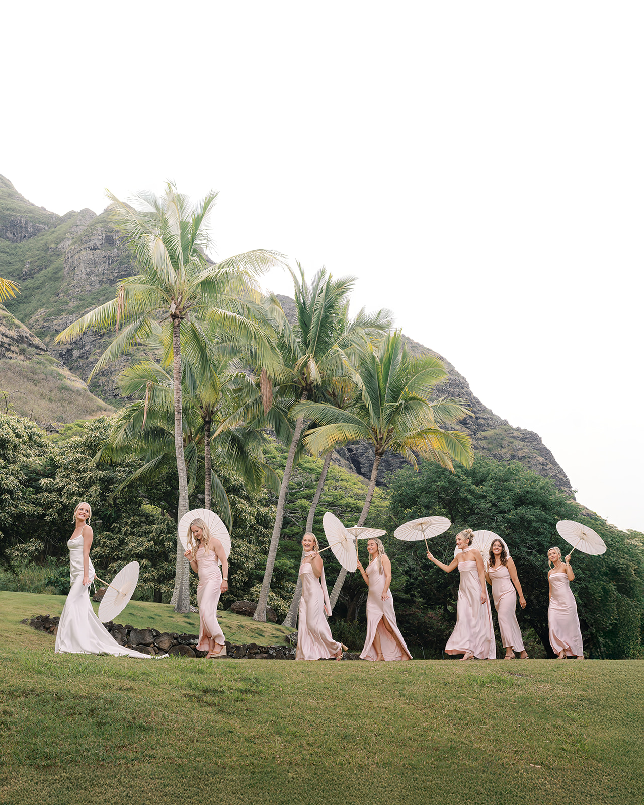 Bridal party walking down a grassy path with parasols at Kualoa Ranch, Paliku Gardens, Oahu.