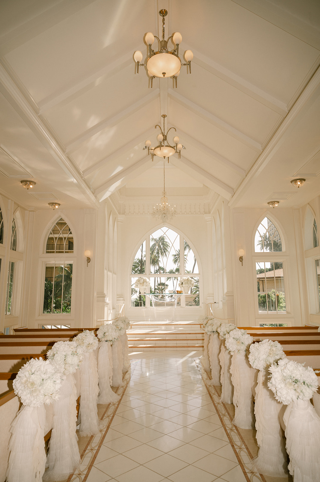 Interior view of Akala Chapel decorated for a wedding ceremony, with white floral aisle arrangements and tropical light streaming through the arched windows — perfect for an elegant Akala Chapel wedding in Waikiki.