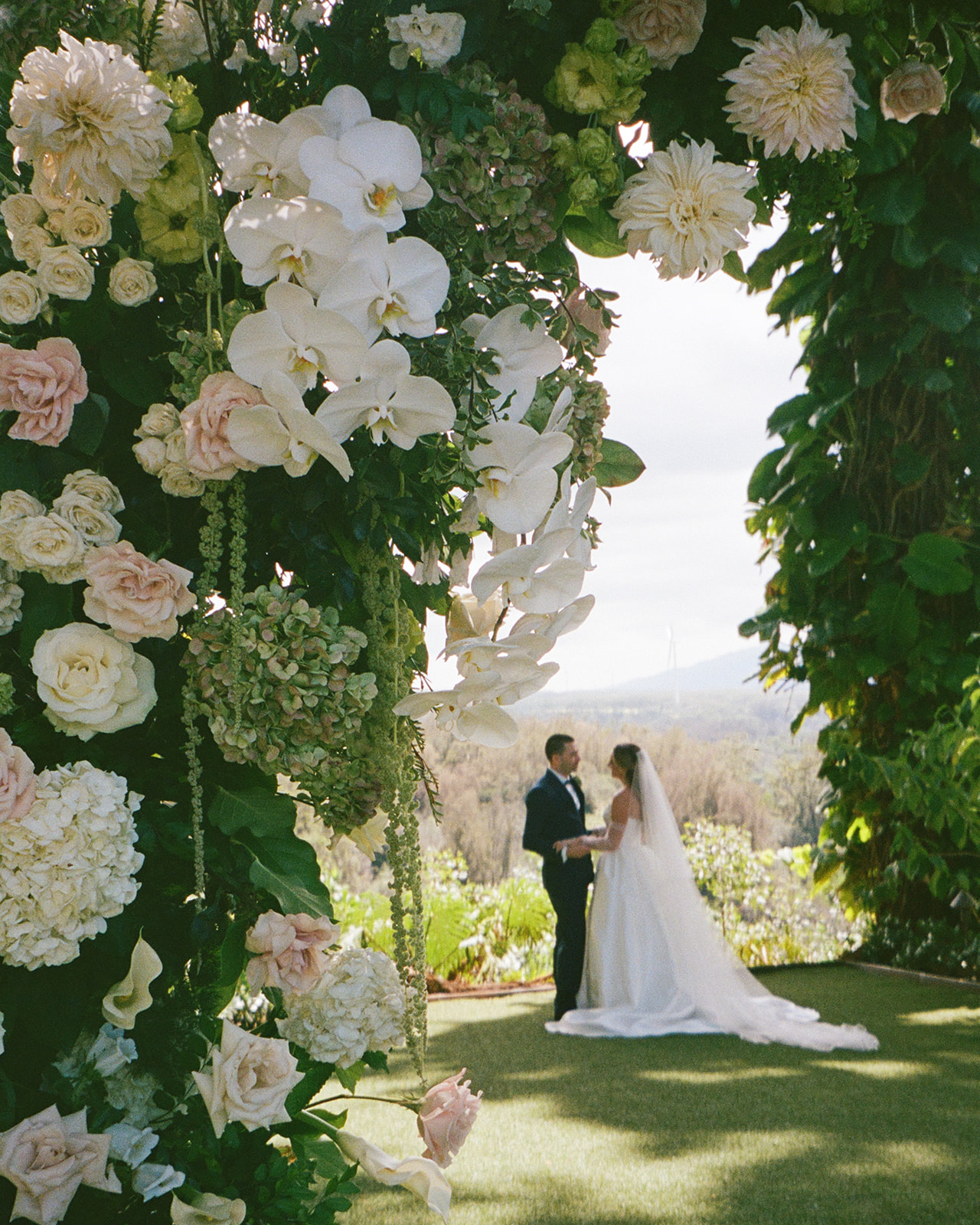 A bride and groom share a quiet moment at Sunset Ranch on Oahu, framed by lush greenery and soft florals during their ceremony, captured as part of a multi-day wedding Hawaii celebration.