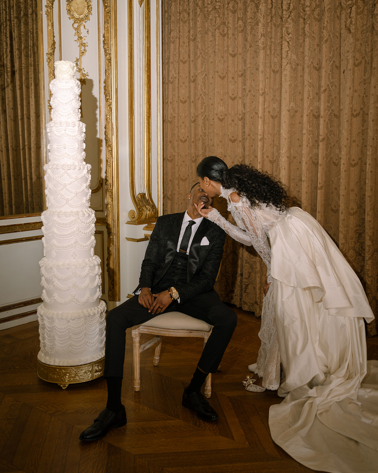 Bride playfully kissing her groom in front of a towering wedding cake at their Brunch Wedding at Ochre Court Newport.
