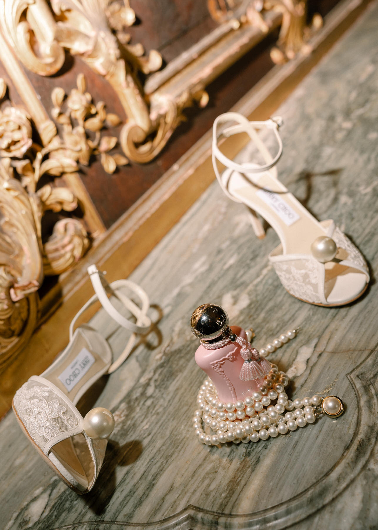 Bridal shoes with pearls and perfume bottle styled elegantly on a marble surface at the wedding.