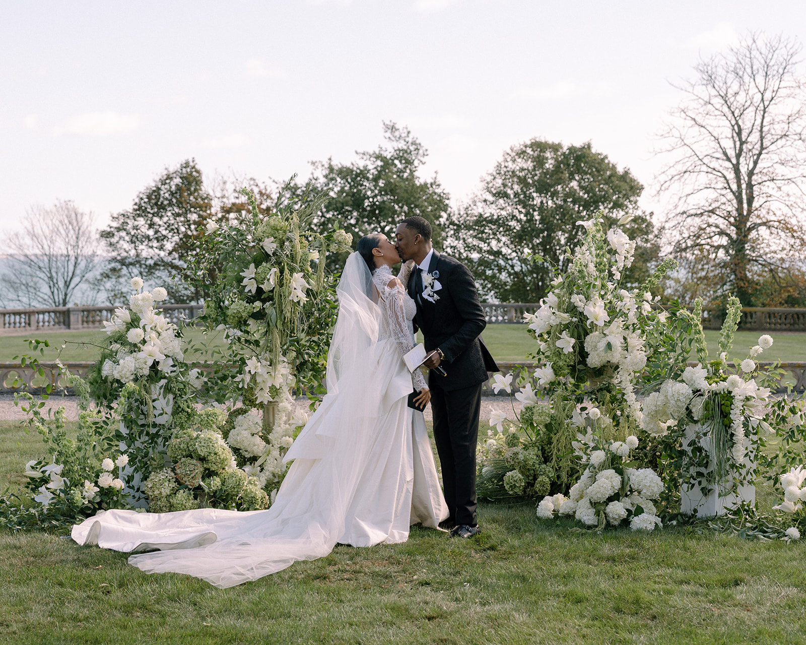 Bride and groom sharing a kiss surrounded by lush white flowers during their Brunch Wedding at Ochre Court Newport.