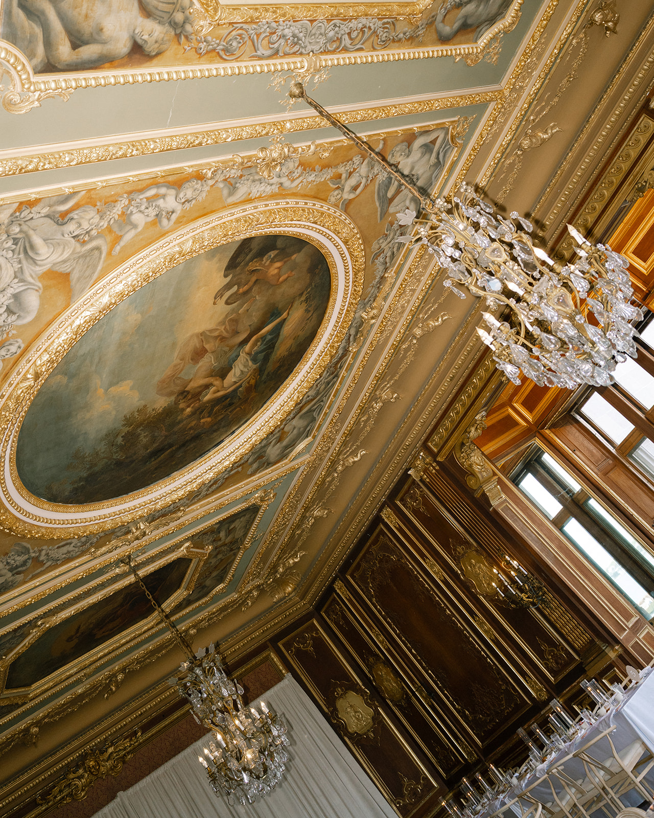 Stunning painted ceiling with crystal chandeliers, capturing the grandeur of the Brunch Wedding at Ochre Court Newport.
