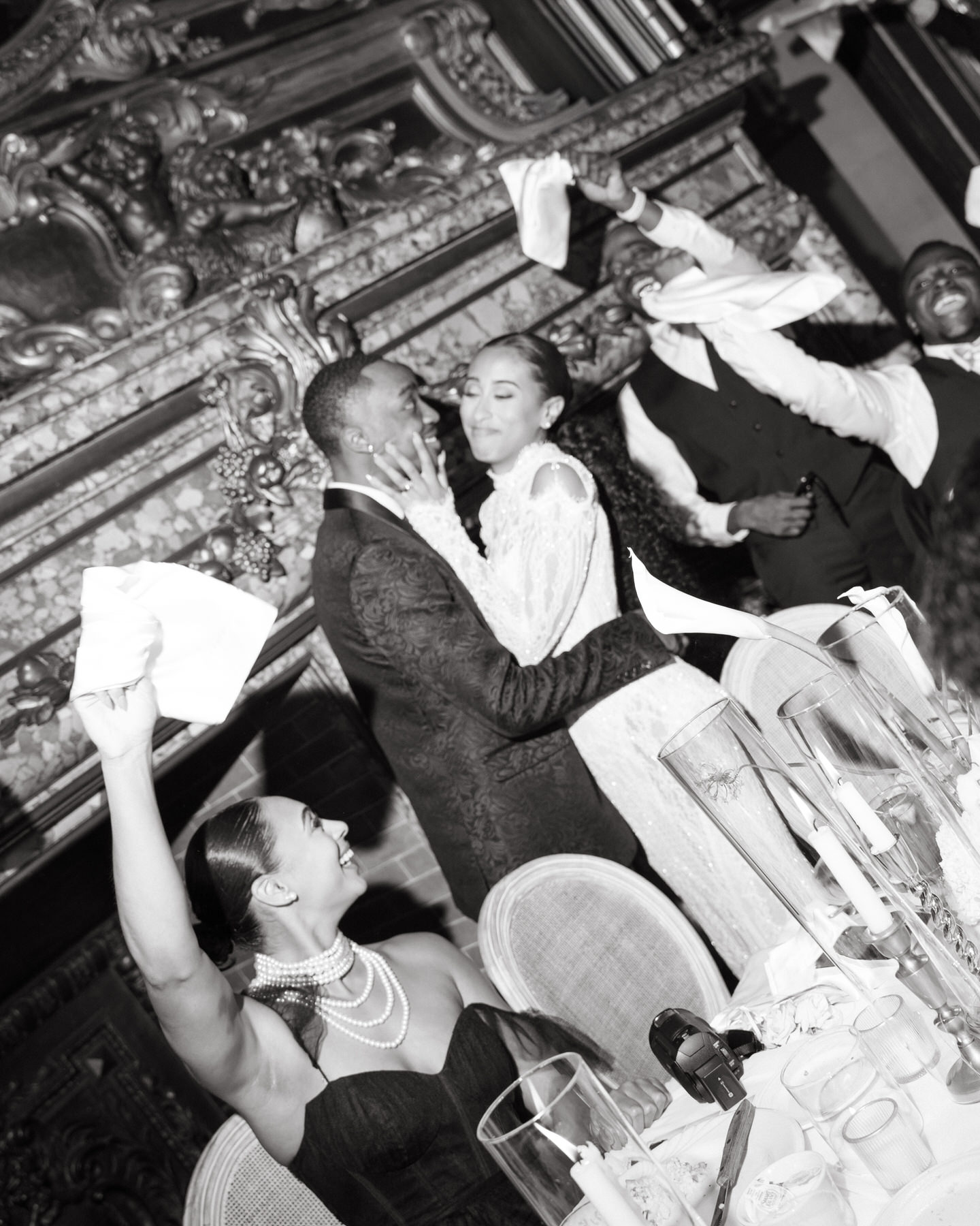 Bride and groom sharing a loving moment at the reception, while guests celebrate and wave napkins during the brunch wedding at Ochre Court Newport.