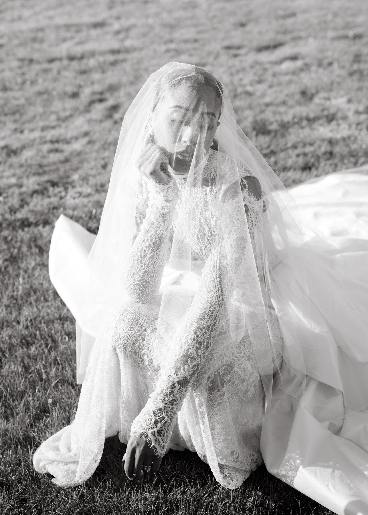 Bride sitting gracefully on the grass, wearing a delicate lace wedding gown with a veil during the brunch wedding at Ochre Court Newport.