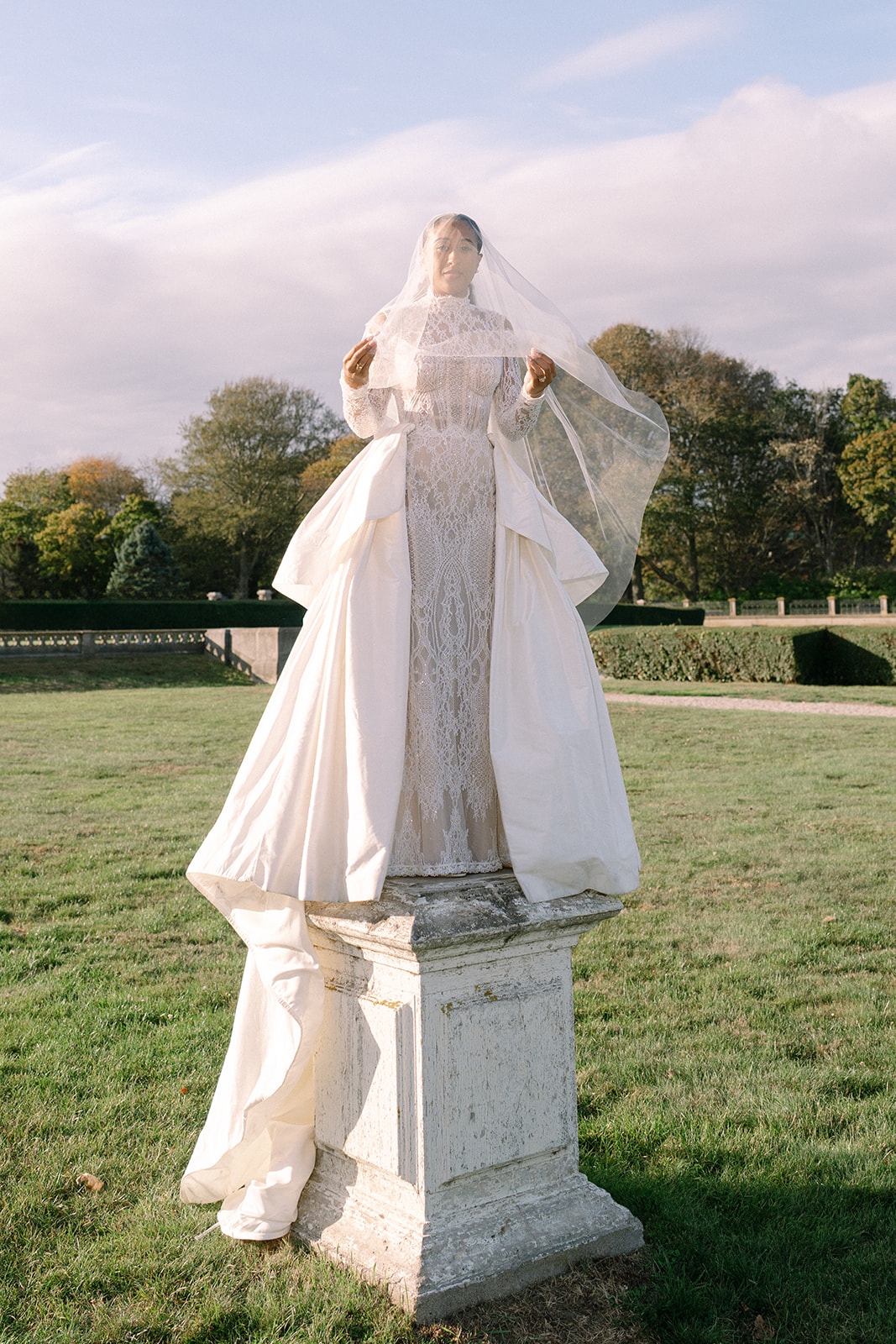Bride standing tall in her stunning wedding dress, veil flowing, in the beautiful outdoor setting of the Brunch Wedding at Ochre Court Newport.

