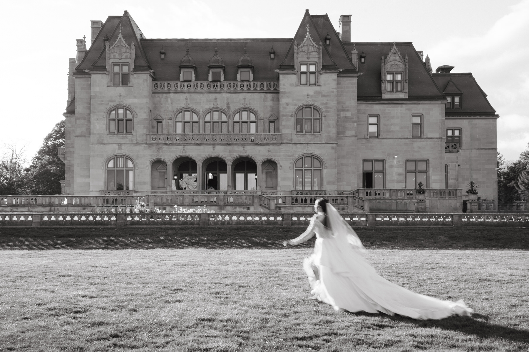 Bride running across the lawn toward the Ochre Court Newport mansion, her flowing gown trailing behind her at the brunch wedding.