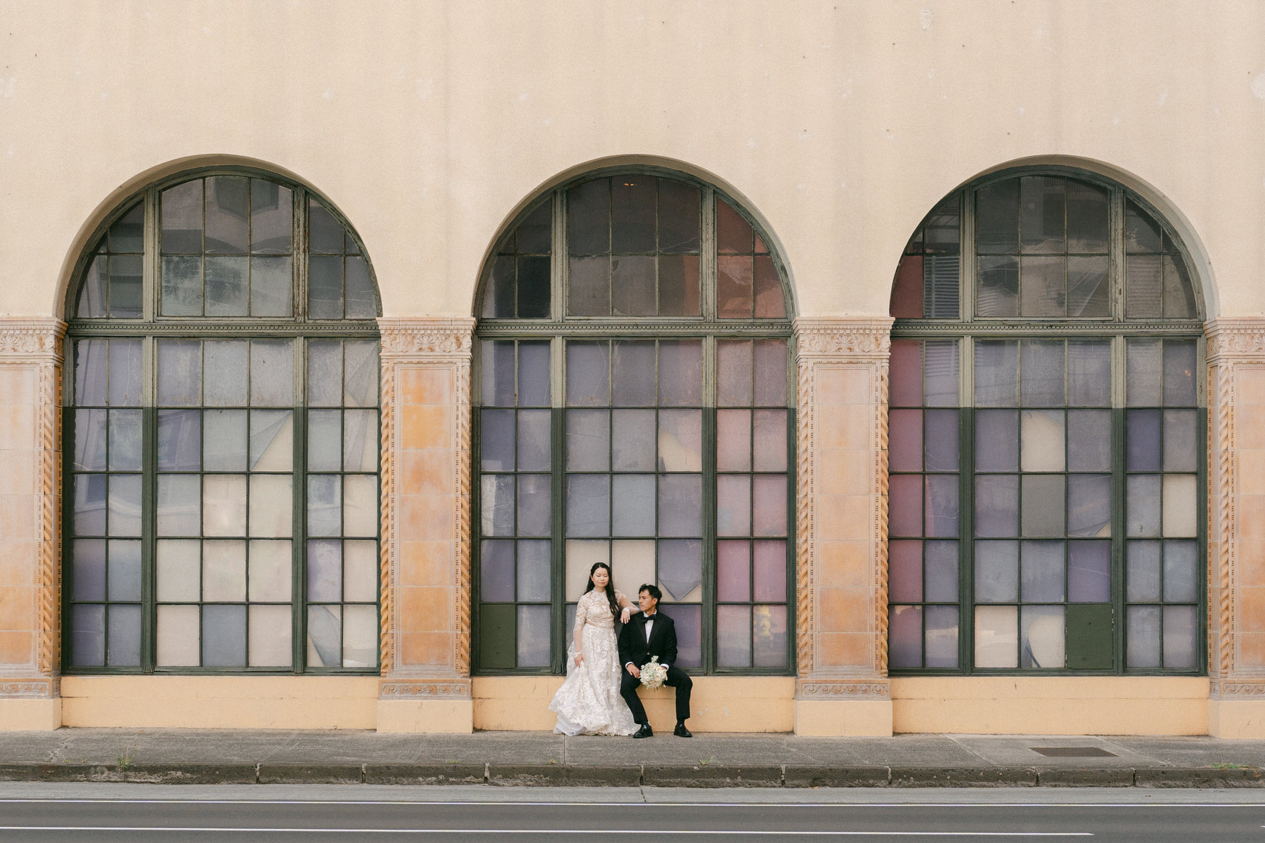 Newlyweds standing beneath tall arched windows near the Cafe Julia Hawaii wedding venue in Honolulu.