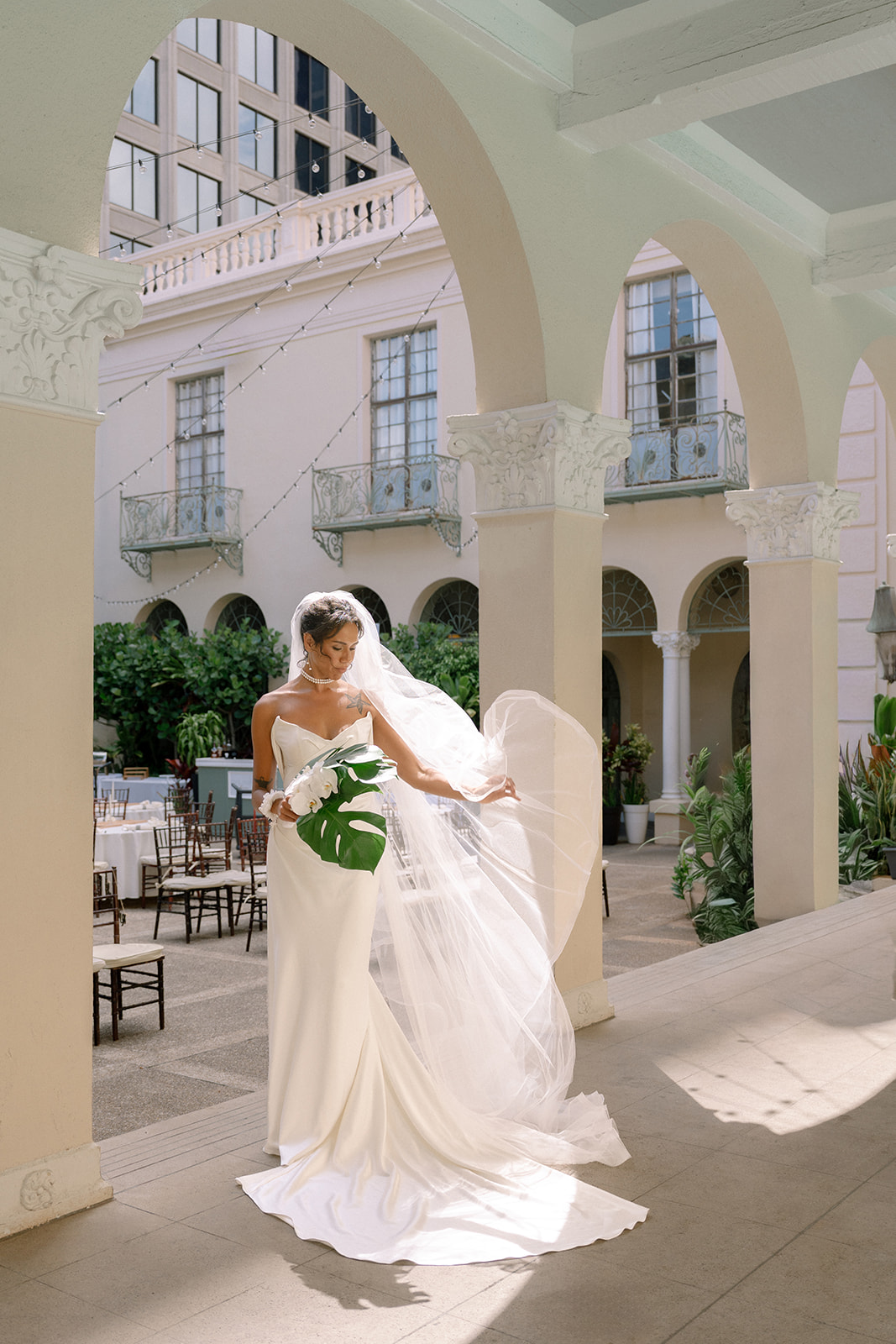 Bride walking through the arched courtyard with a white bouquet at Cafe Julia in Honolulu.