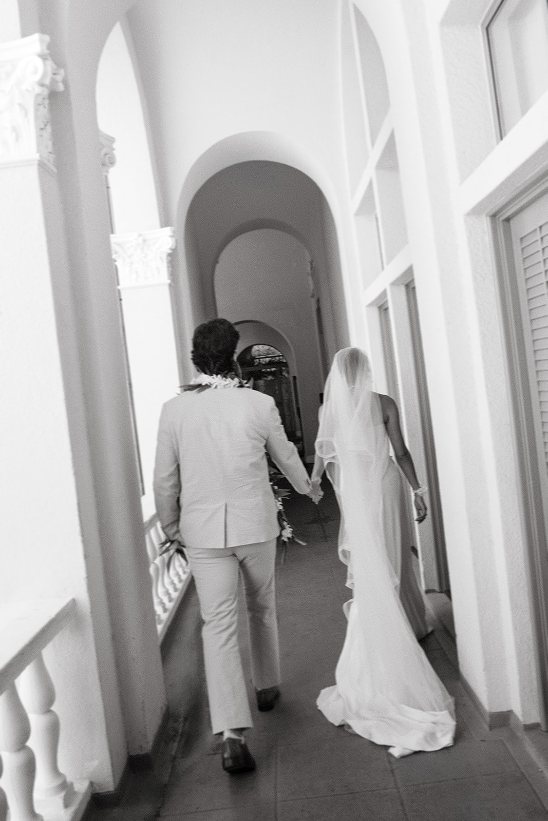 Newlyweds walking hand in hand through an arched corridor at Cafe Julia in Honolulu.
