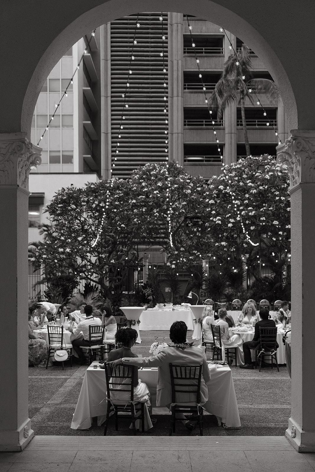 Black-and-white view of guests dining in the Cafe Julia courtyard, framed by a historic archway.