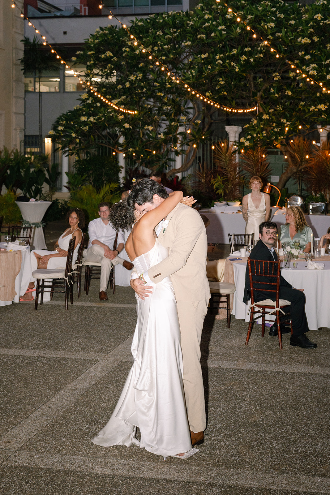 Newlyweds kissing beneath string lights during their Cafe Julia courtyard wedding reception.