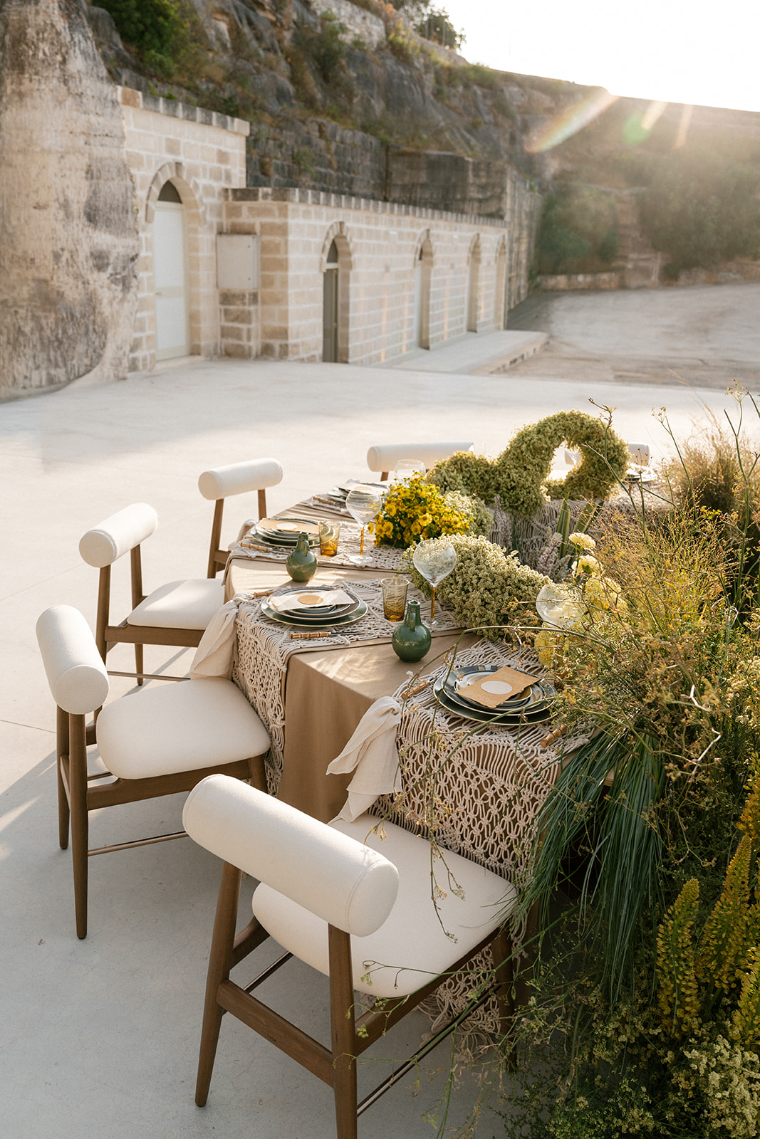 Curved reception table with layered place settings, yellow florals, and greenery at Cava Puglia.