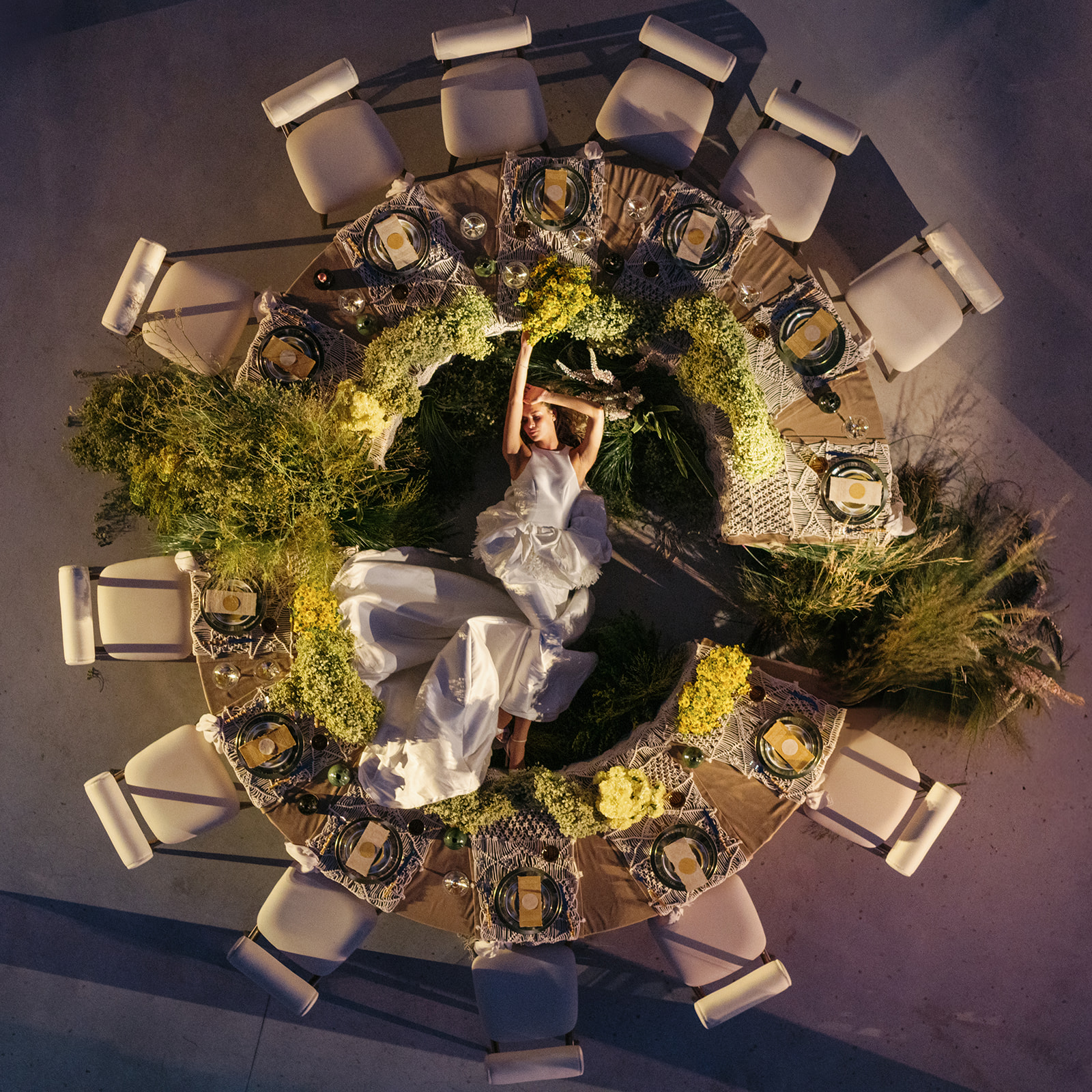Overhead view of a bride reclining within a circular, flower-filled reception table at Cava Puglia.