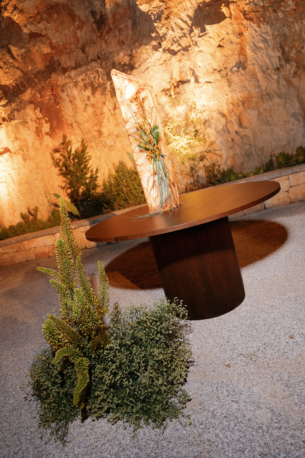 Sculptural wooden table and botanical arrangement set against illuminated limestone at Cava Puglia.