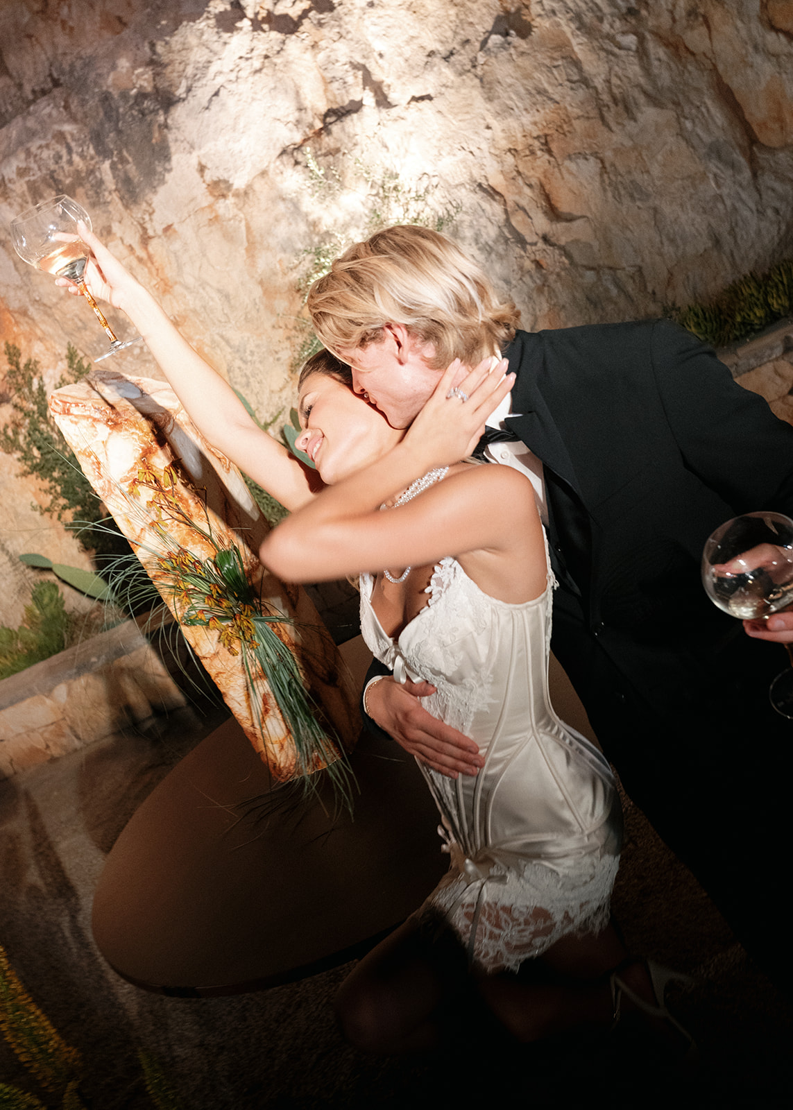 Newlyweds kiss beside sculptural reception décor and illuminated limestone walls at Cava Puglia.