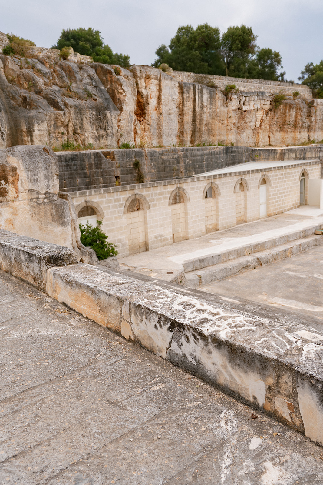 Tiered limestone terraces and arched stone walls define the open-air setting at Cava Puglia.