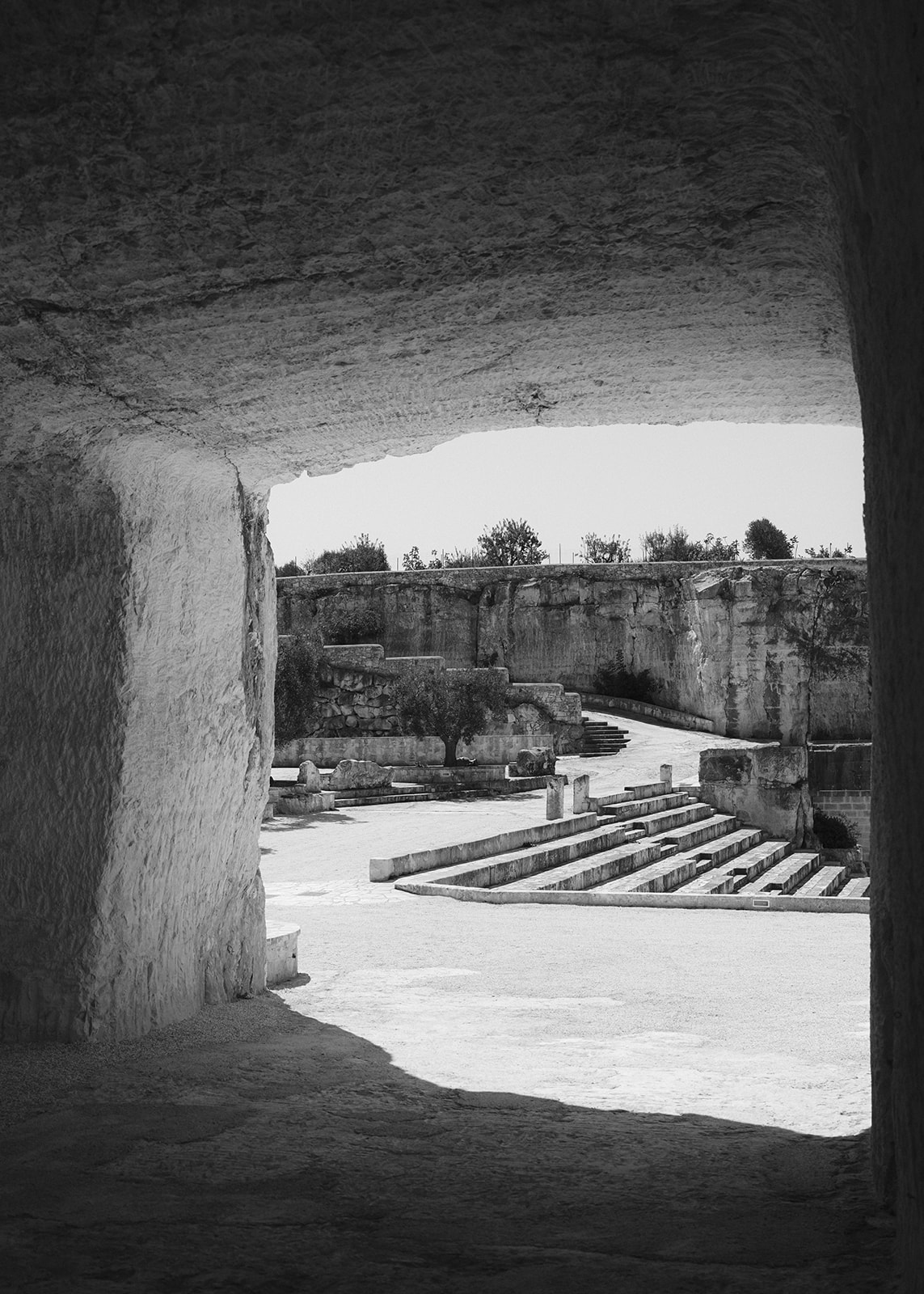 Black-and-white view through a carved stone passage toward the amphitheatre at Cava Puglia.