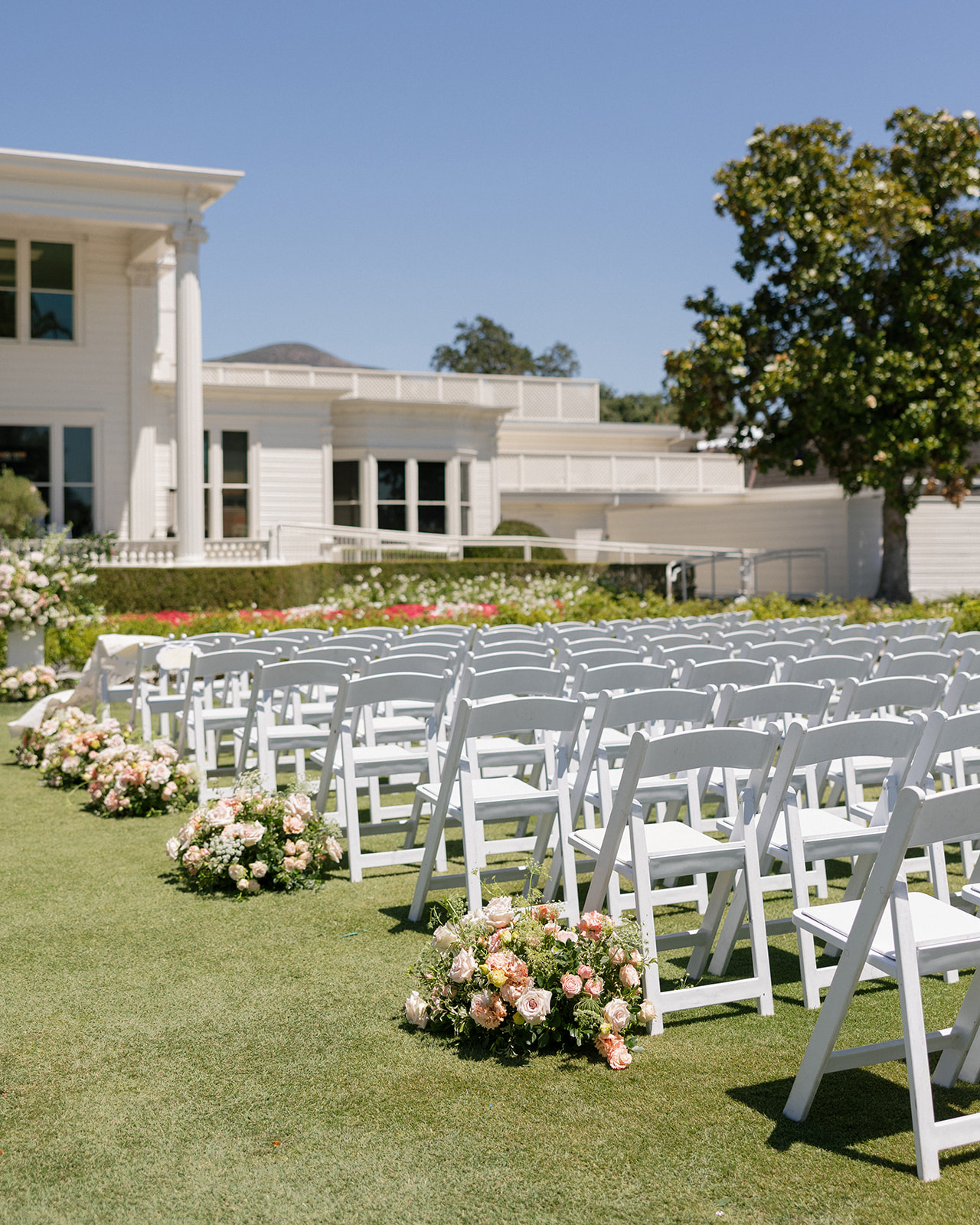 White ceremony chairs and low pastel floral arrangements line the lawn at Silverado Resort in Napa.
