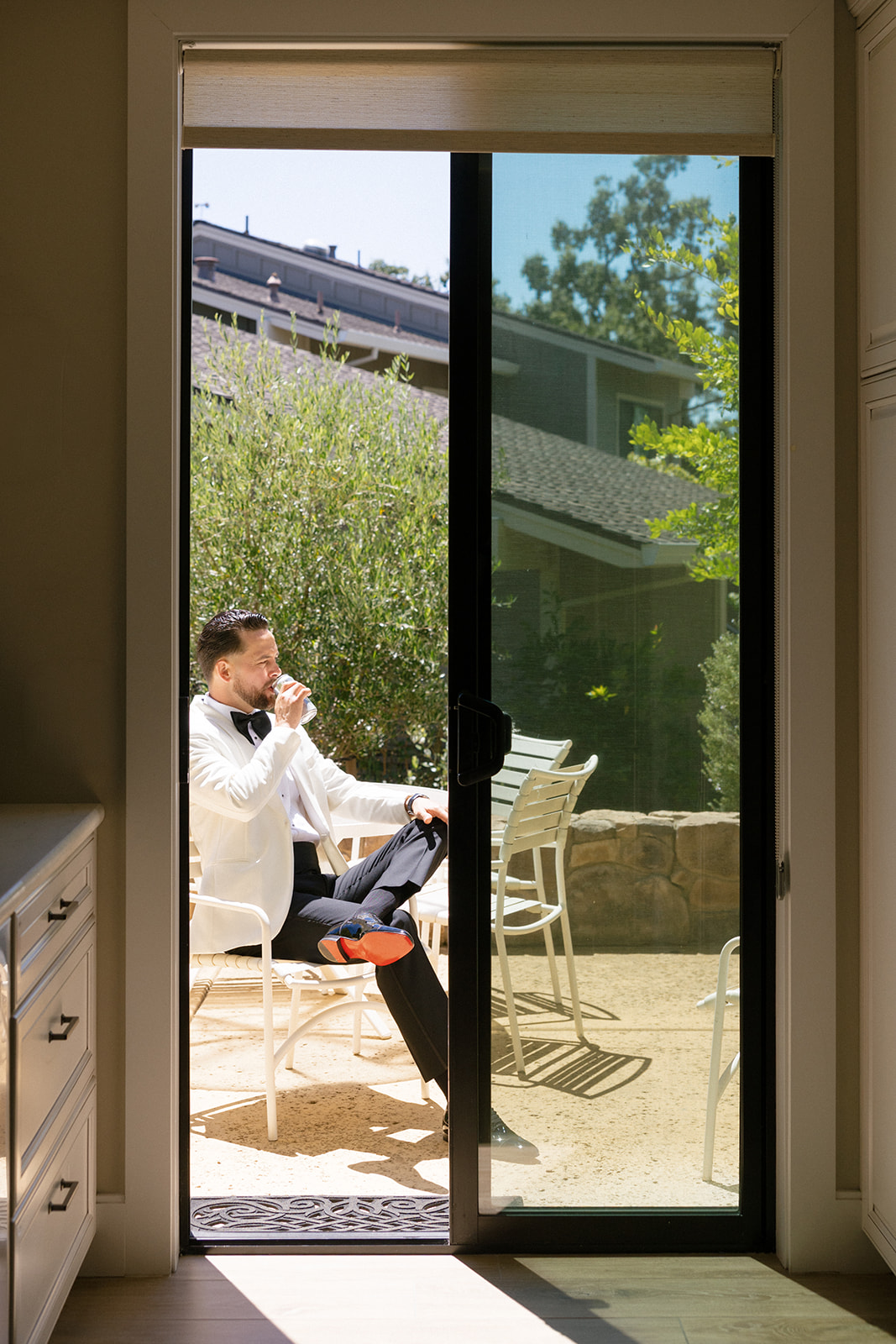 Groom sits on a sunlit patio framed by a sliding glass door at Silverado Resort in Napa.