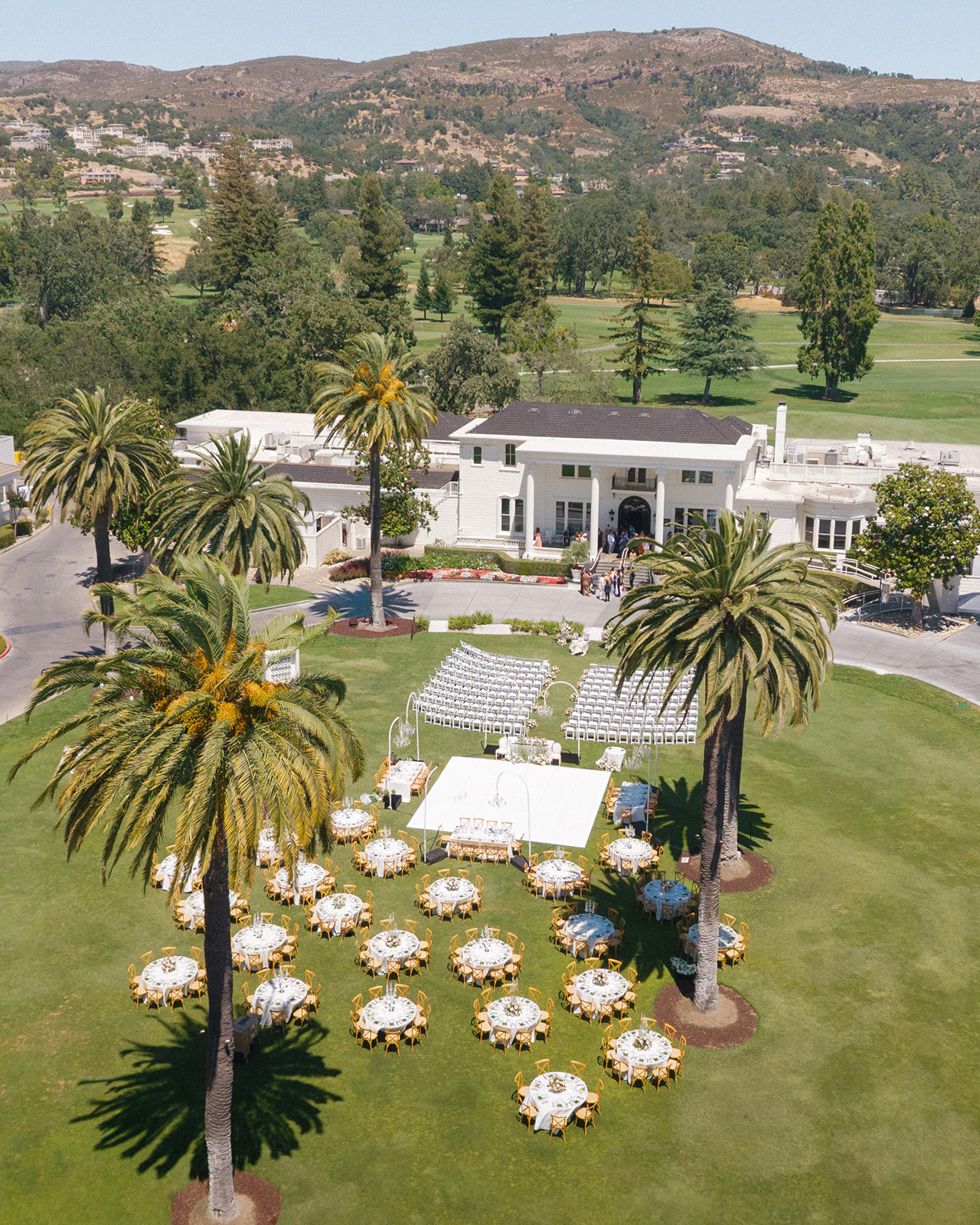 Aerial view of an outdoor wedding ceremony and reception on the palm-lined lawn at Silverado Resort in Napa, with the resort mansion, golf course, and hills beyond.