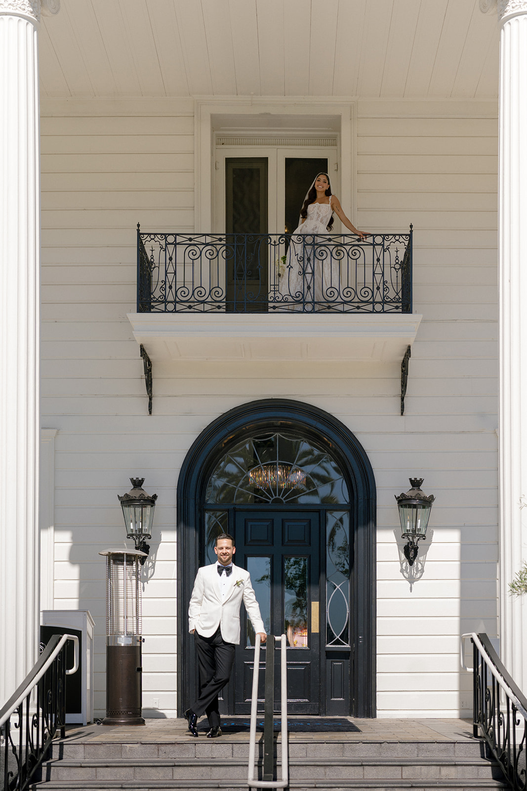 Bride stands on a balcony above the groom at the mansion entrance of Silverado Resort in Napa.