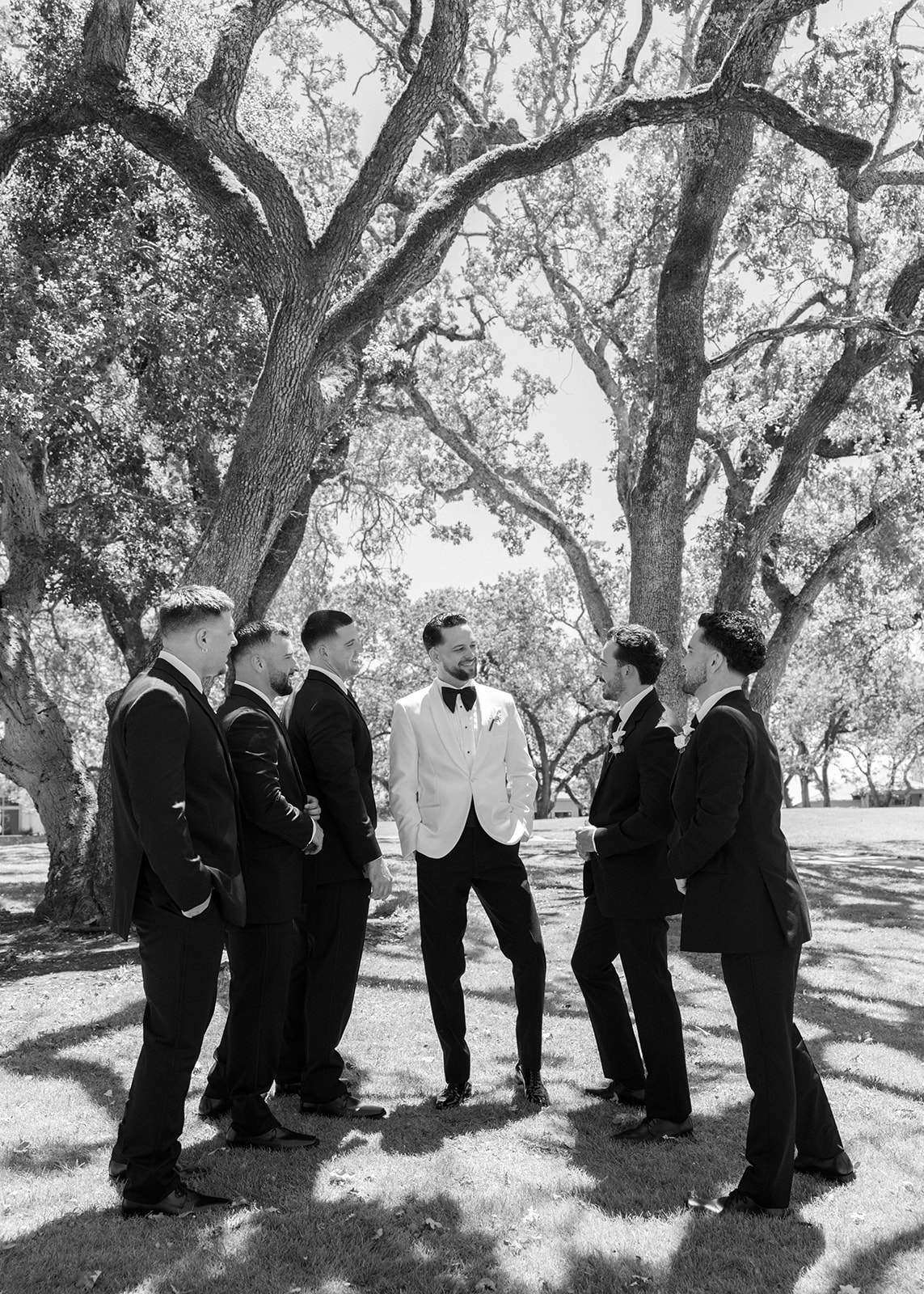 Groom in a white dinner jacket stands with groomsmen beneath an oak tree at Silverado Resort in Napa.
