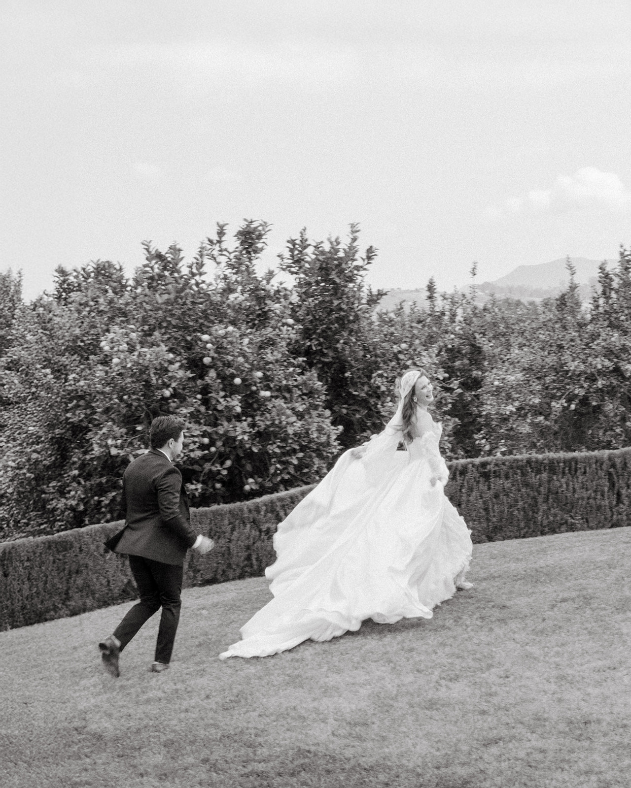 Black-and-white photo of the bride and groom running across the lawn at Villa Amodei.