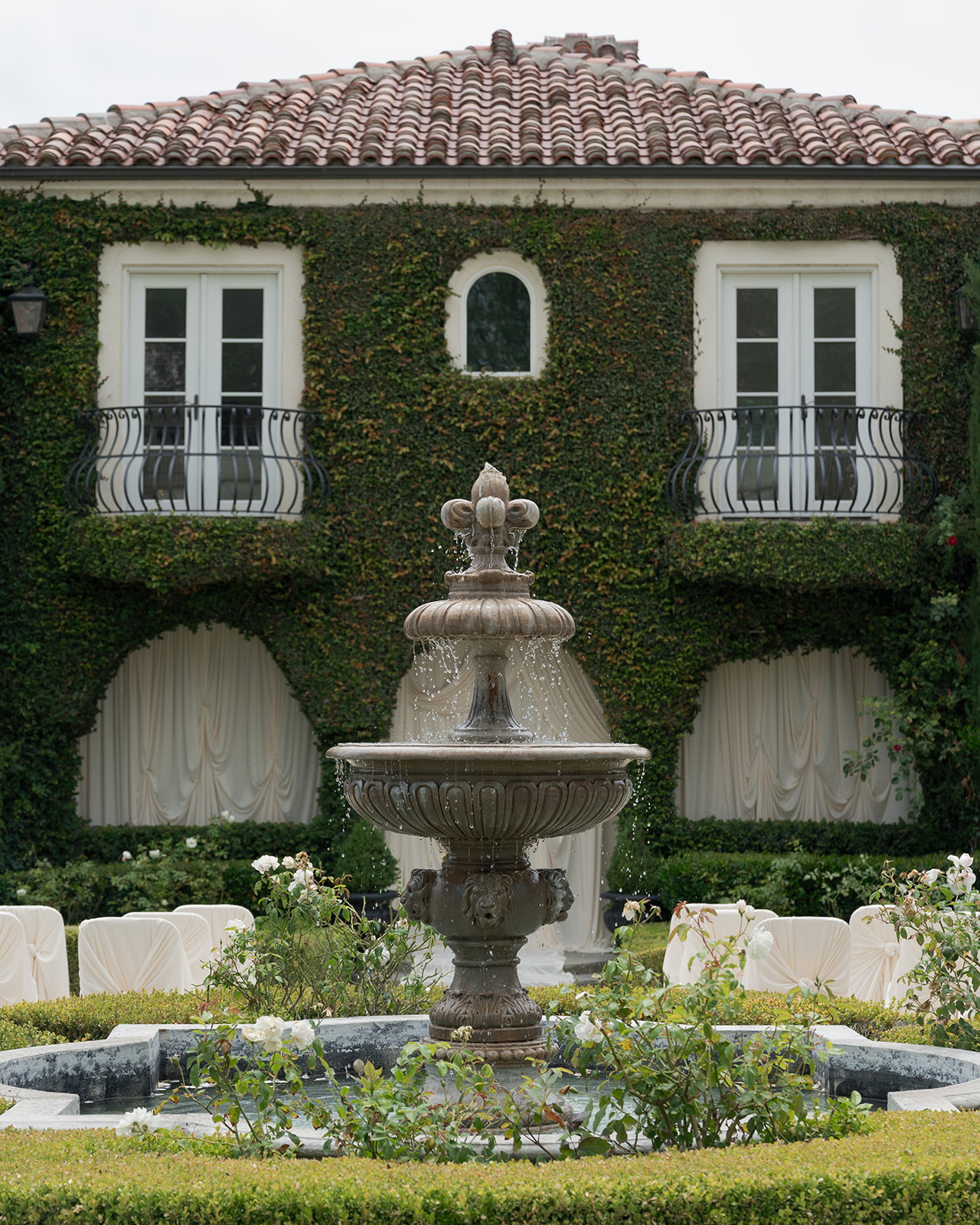 Tiered stone fountain in front of Villa Amodei’s ivy-covered facade and wrought-iron balconies.