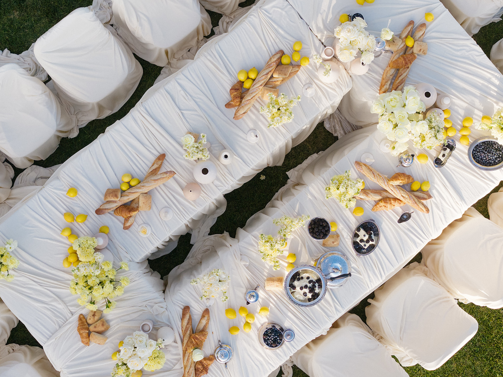 Overhead view of wedding tables at Villa Amodei with white linens, yellow flowers, lemons, and baguettes.